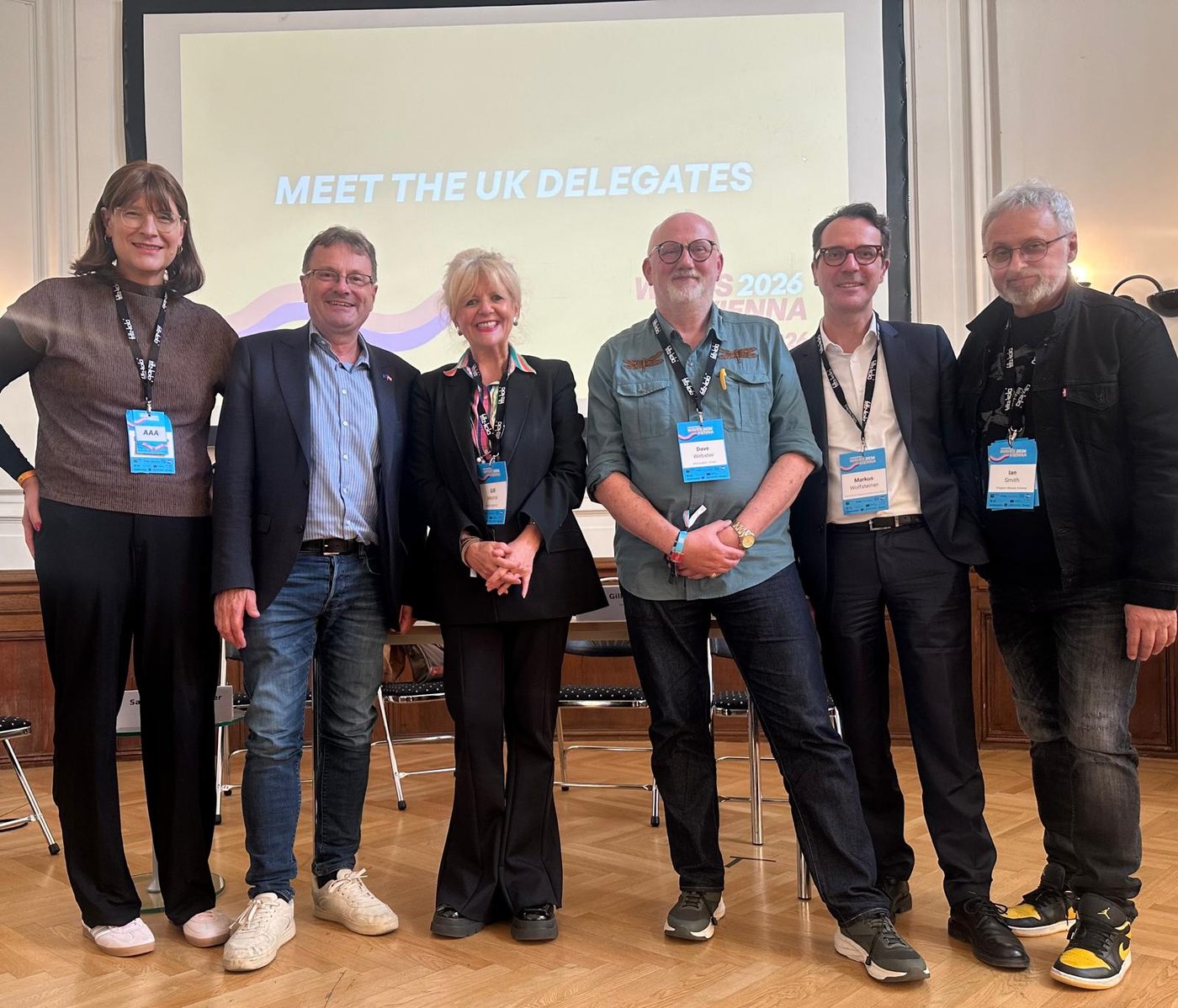 Gill Morris and Ian Smith with fellow speakers in front of a screen reading Meet the UK Delegates at Waves Vienna 2026